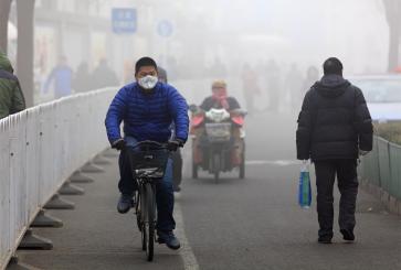 Man wearing a face mask rides a bicycle on a foggy day.