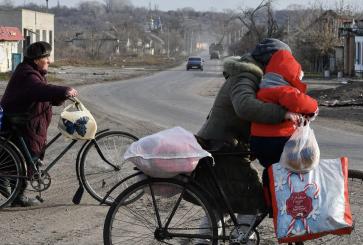 People dressed in warm clothes on bicycles carrying reusable shopping bags.